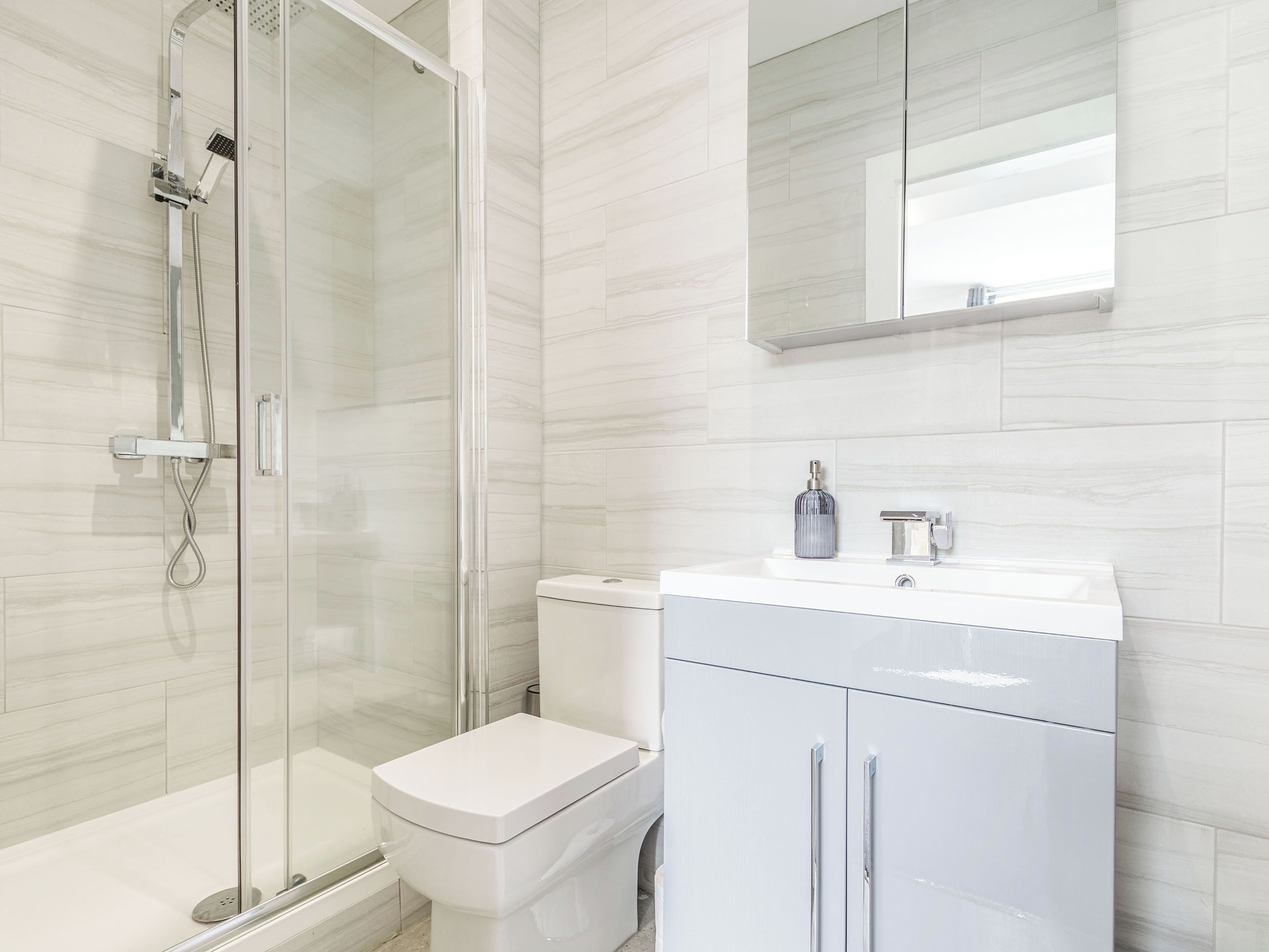 A modern bathroom with a glass-enclosed shower, a white toilet, and a white vanity with a mirror.