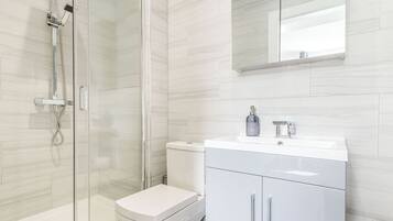 A modern bathroom with a glass-enclosed shower, a white toilet, and a white vanity with a mirror.