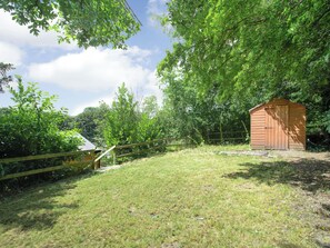 A wooden shed in a grassy area with trees in the background.