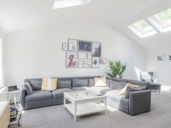 A modern living room with a grey sofa, a glass coffee table, and a skylight.