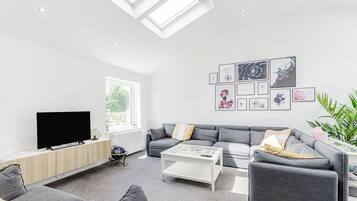 A modern living room with a grey sofa set, a flat-screen TV, a coffee table, and a skylight.