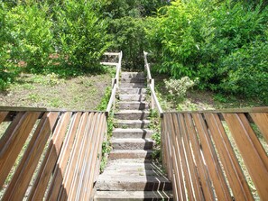 A wooden staircase leading up to a wooden deck surrounded by greenery.
