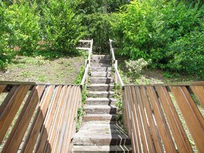 Una escalera de madera que conduce a una terraza de madera rodeada de follaje.
