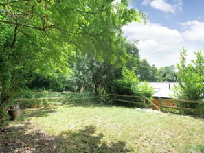 A fenced outdoor area with grass, trees, and a building in the background.