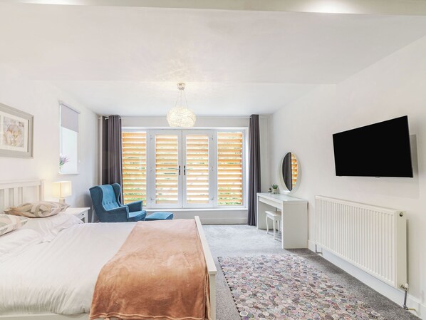 A bedroom with a bed, a chair, a desk, a television, and a window with blinds.