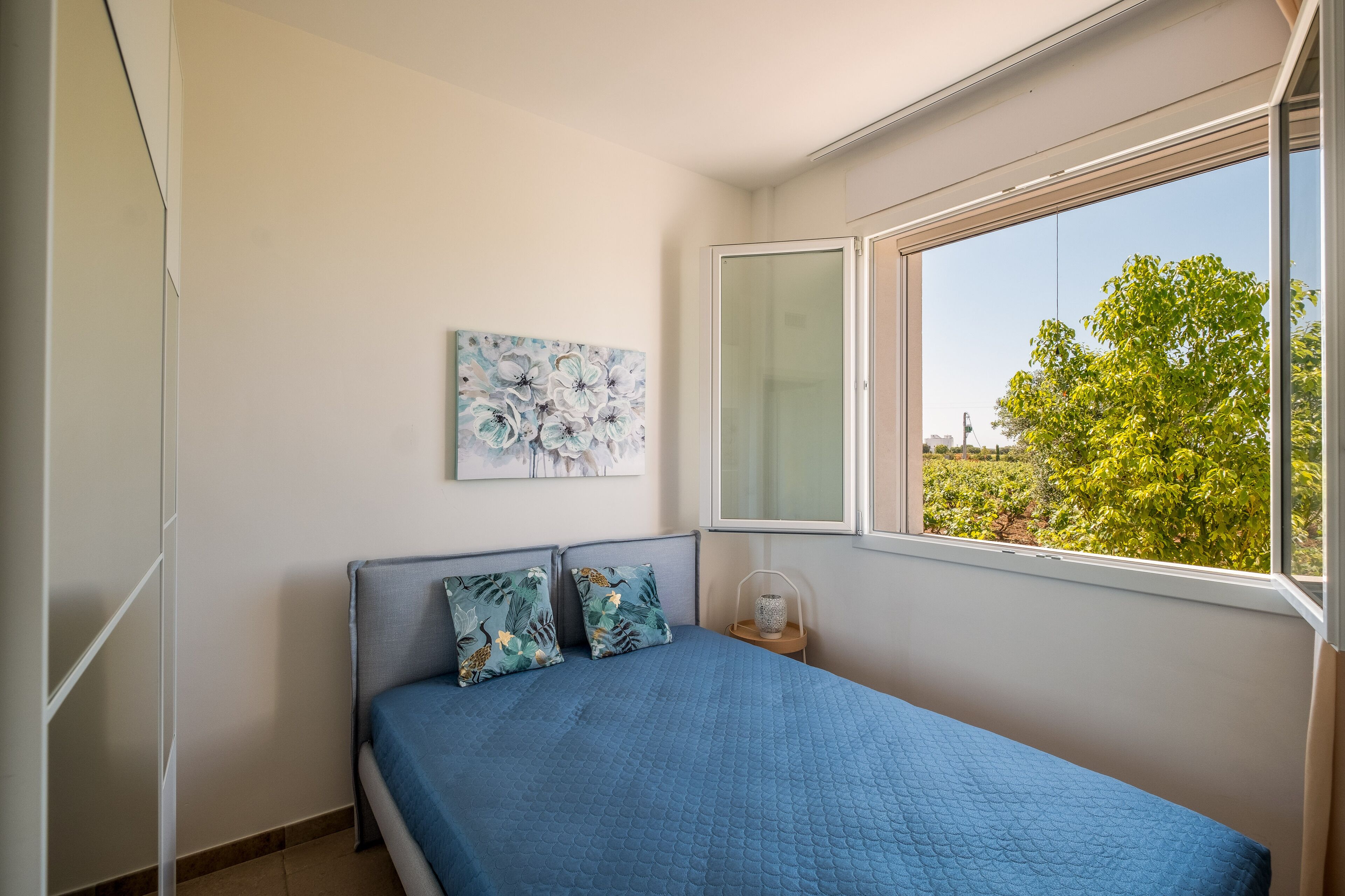 A bedroom with a bed, a window, and a painting on the wall.