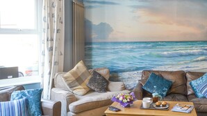 Ett vardagsrum med två soffor, ett soffbord och en väggmålning som föreställer havet.