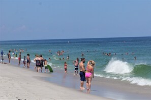 A crowded beach with people walking and swimming in the water.