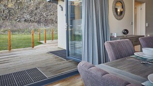 Une chambre moderne dotée d’une porte vitrée donnant sur un balcon, d’un coin repas avec une table et des chaises, et d’un grand miroir mural.