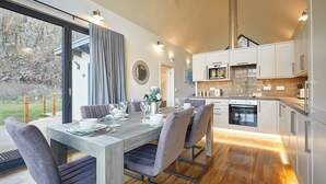 Une cuisine moderne avec des meubles blancs, un four encastré et un coin repas comprenant une table en bois et des chaises à revêtement gris.