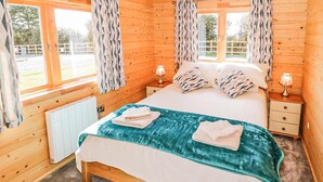 Ein Schlafzimmer einer Holzhütte mit einem Bett, zwei Nachttischen, einem Heizkörper und Vorhängen.