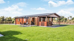 Eine Holzhütte mit überdachter Terrasse, einem Rasen und einem Holzzaun im Hintergrund.