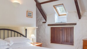 A bedroom with a bed, a nightstand, a lamp, a wooden door, and a skylight.