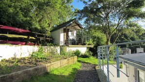 A small house with a balcony, surrounded by greenery and trees.