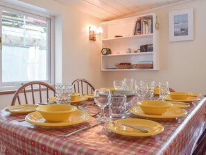 A dining table set with yellow plates and clear glasses, a checkered tablecloth, and a bookshelf with books and decorative items. - 3 bedroom accommodation in Lower Town, Fishguard (Lower Town, Fishguard)