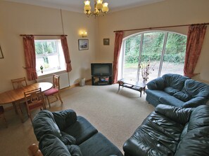 A living room with a sofa, a television, a dining table with chairs, and large windows with curtains. - 3 bedroom accommodation in Wooler (Wooler)
