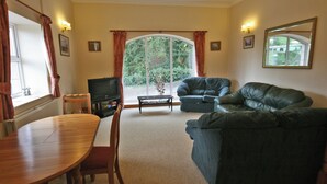 A living room with a dining table, two sofas, a TV, and a large window with curtains.