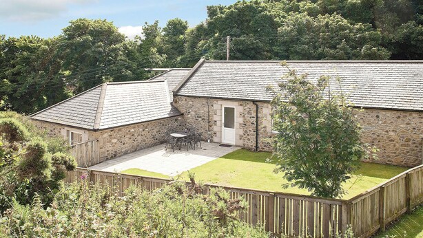 A stone building with a tiled roof, a fenced patio, and a grassy yard.
