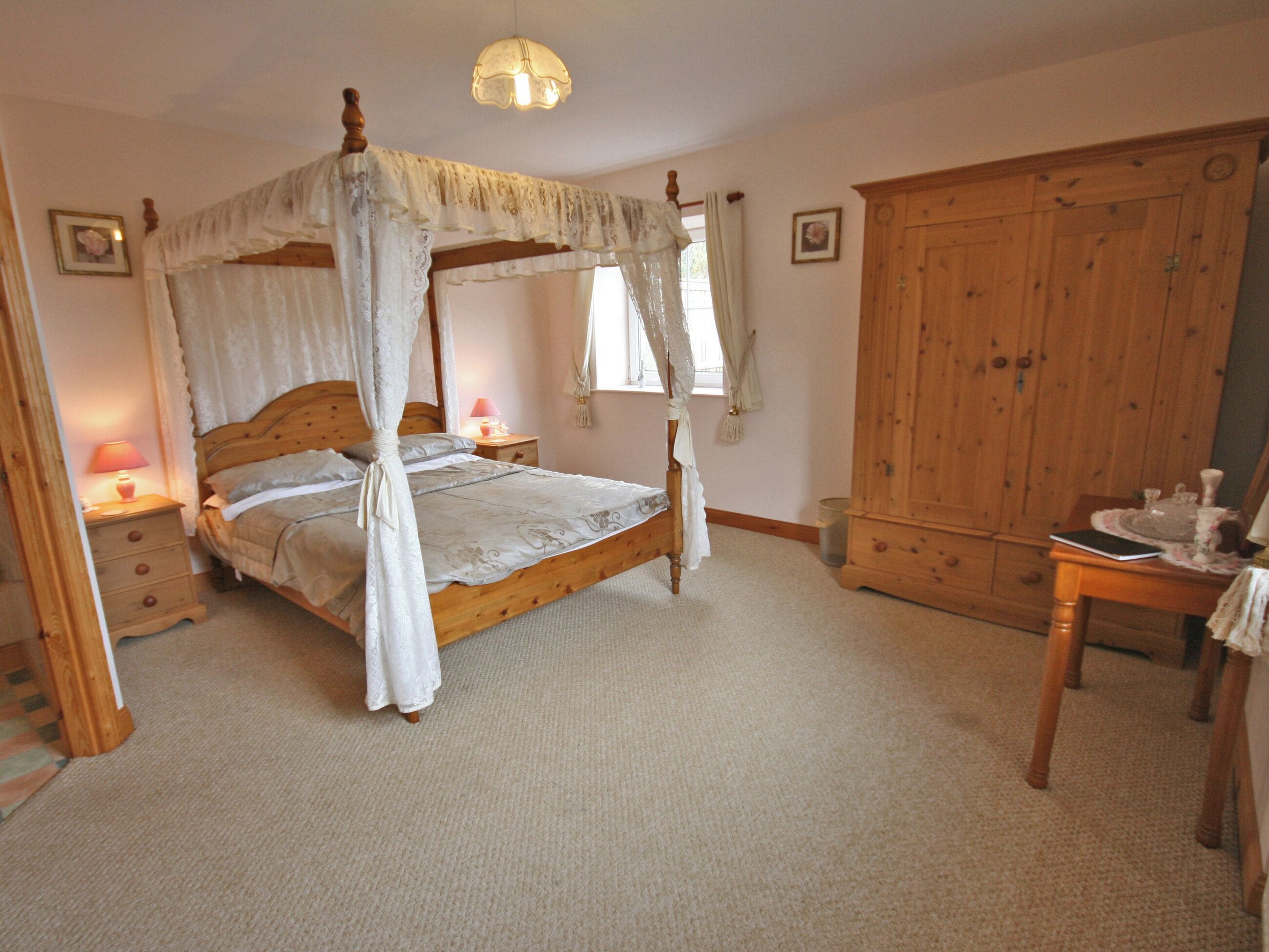 A four-poster canopy bed with a wooden headboard, a bedside table with a lamp, and a wooden wardrobe.