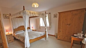 A four-poster canopy bed with a wooden headboard, a bedside table with a lamp, and a wooden wardrobe.