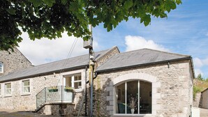 A stone building with a large arched window, a staircase leading to a balcony, and a gravel driveway.