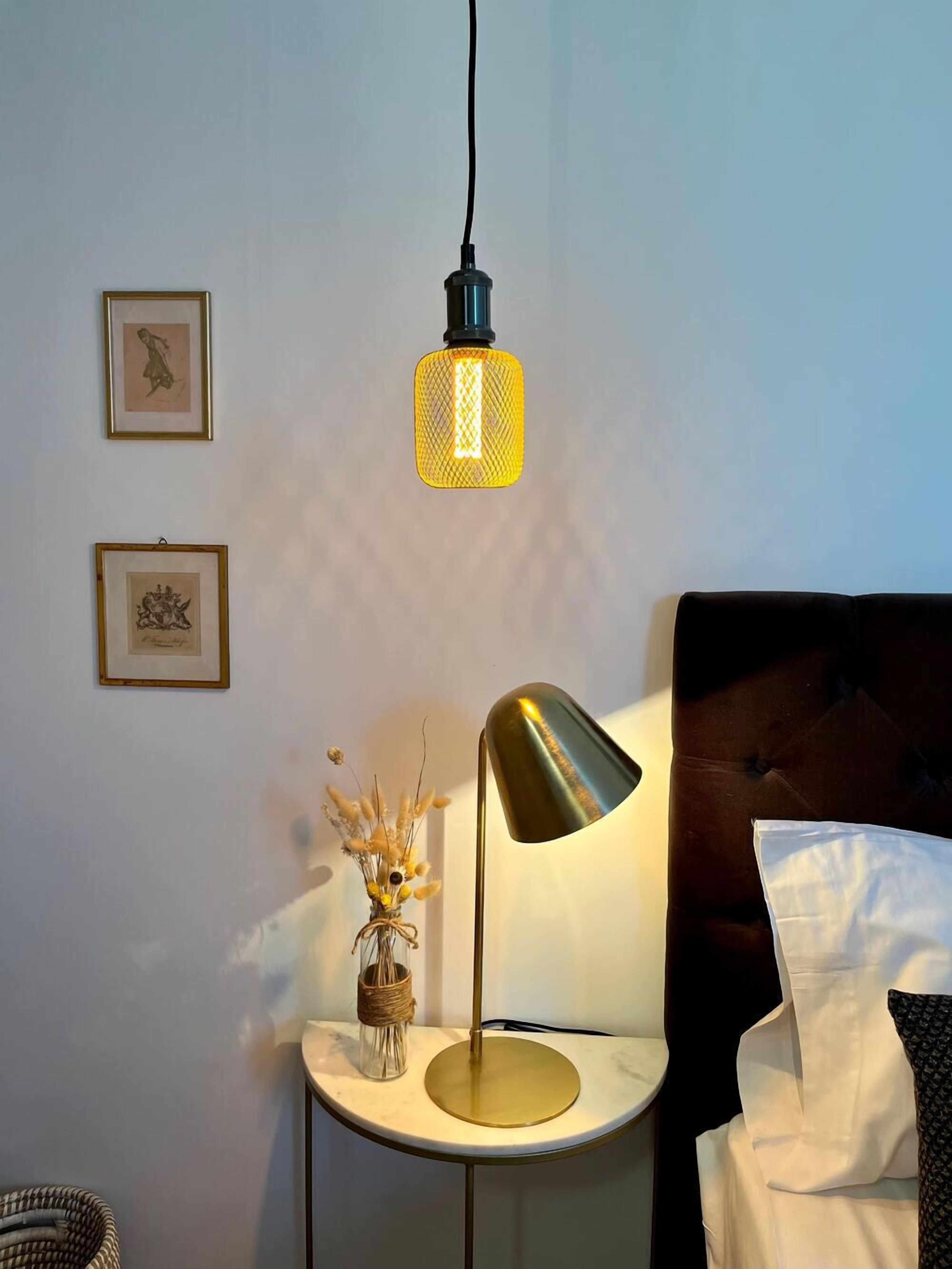 Un dormitorio con una cama, una mesita de noche con lámpara y cuadros enmarcados en la pared.