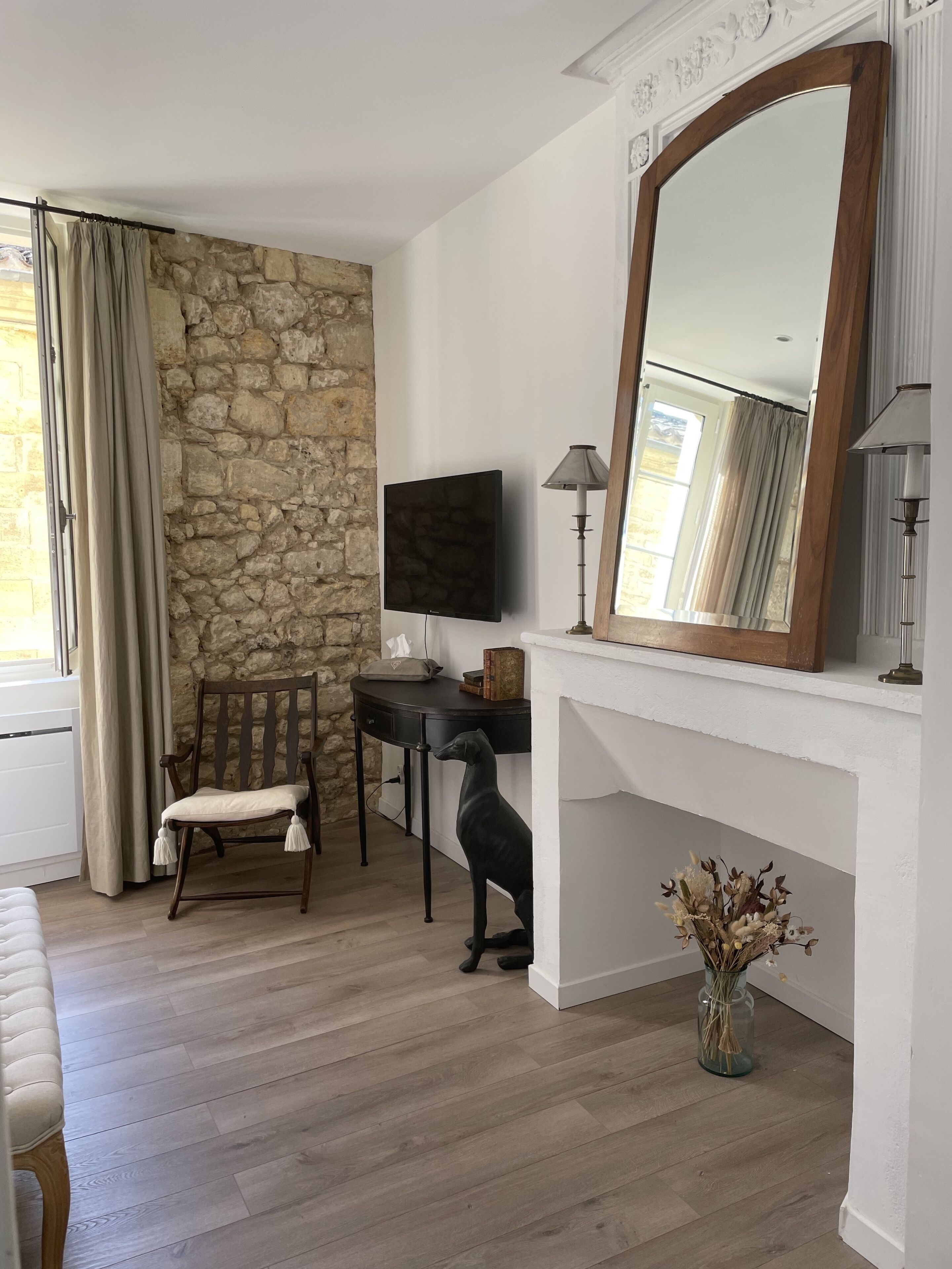 Une pièce avec un mur en pierre, une chaise en bois, un téléviseur, une lampe et un vase contenant des fleurs séchées.