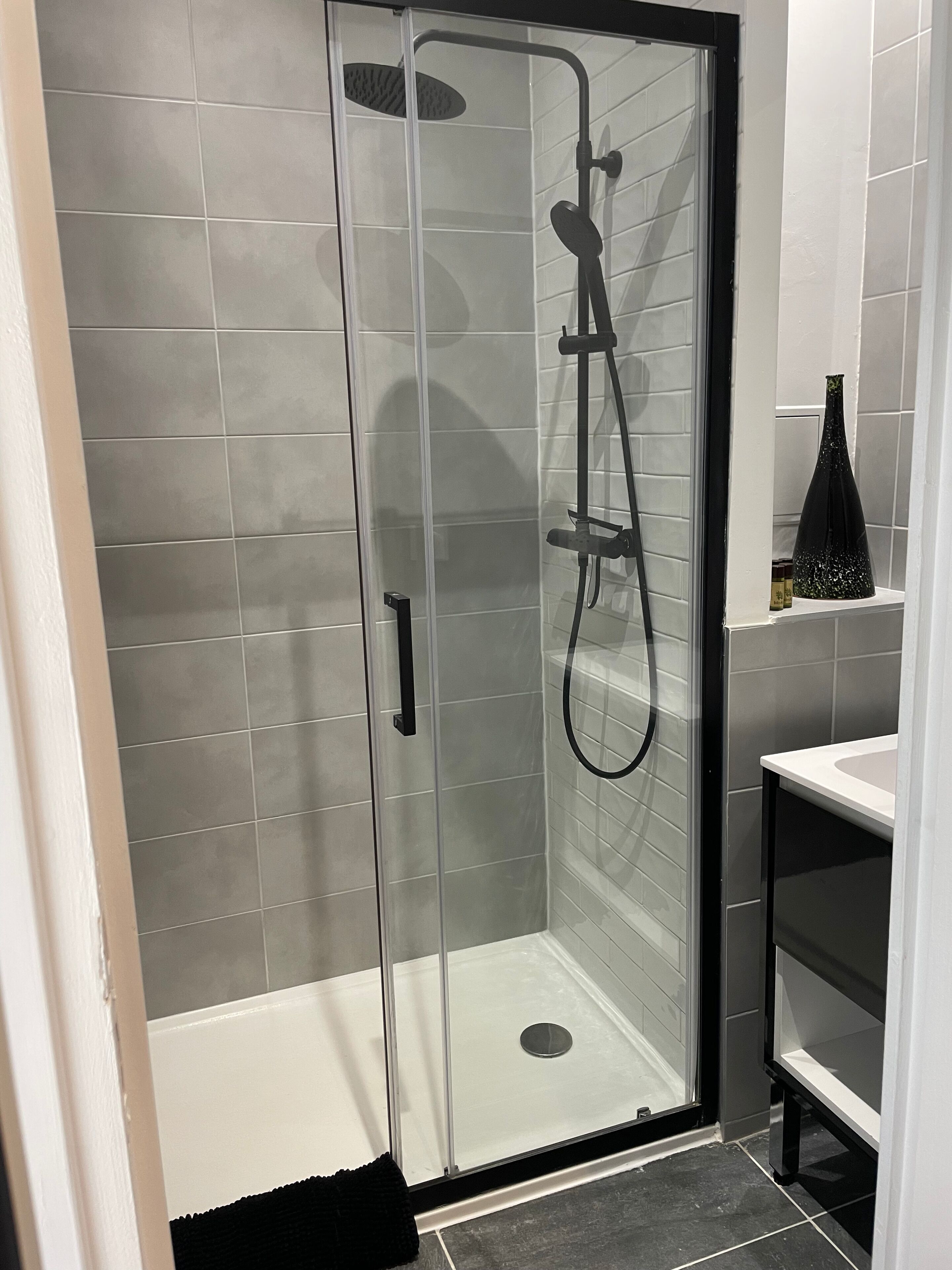Une douche fermée par des parois en verre, dotée d’un pommeau de douche à main et d’un robinet mural.