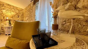Una habitación acogedora con pared de piedra, un sofá verde, una mesita redonda con una bandeja que contiene vasos y una escultura decorativa de un pájaro.