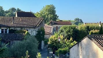 A narrow alleyway with stone walls and tiled roofs, surrounded by greenery and trees.