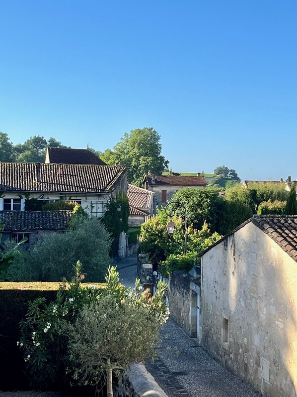 A narrow alleyway with stone walls and tiled roofs, surrounded by greenery and trees. - La Maison du Clocher (Saint-Émilion)
