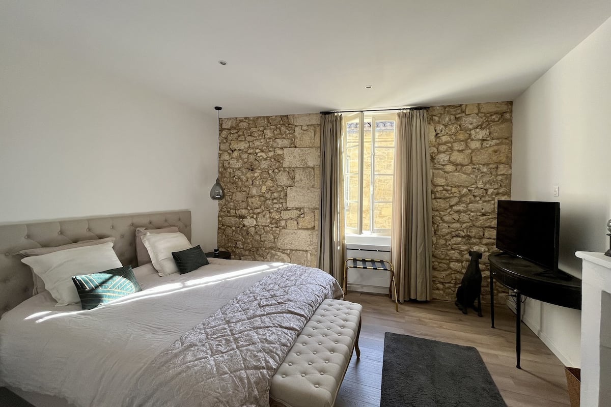 A bedroom with a large bed, stone wall, and a television on a stand.