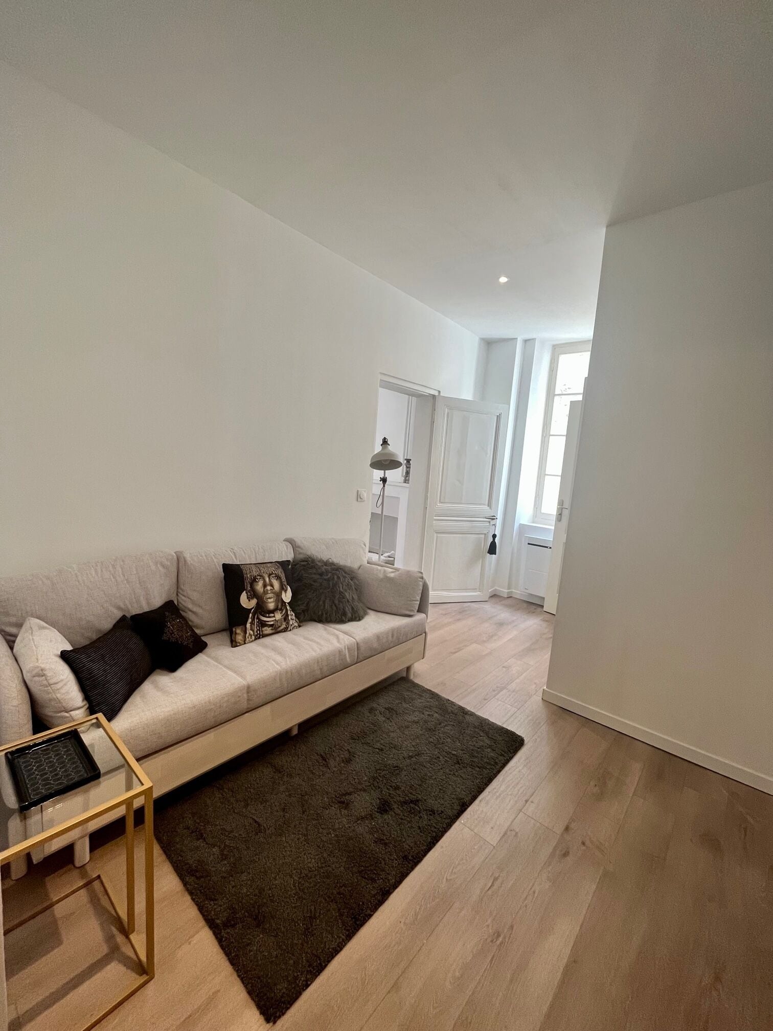 Een moderne woonkamer met een lichtgekleurde bank, een donker vloerkleed en een glazen salontafel.