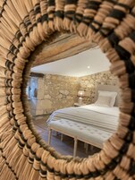 Un dormitorio con pared de piedra, cama con almohada estampada y lámpara de noche.