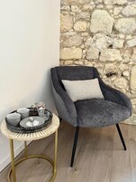Un sillón tapizado en gris con un cojín, colocado junto a una mesita redonda con una bandeja estampada.
