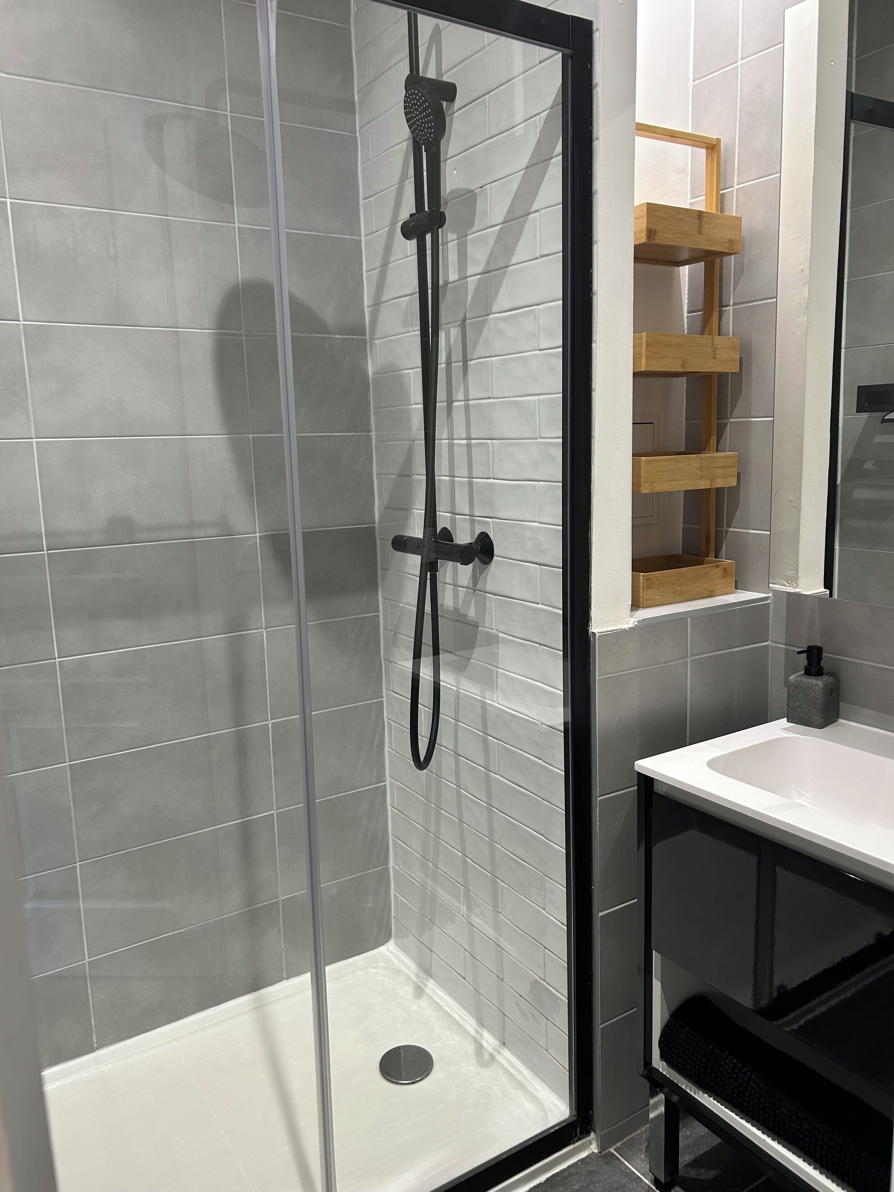 Ein modernes Badezimmer mit einer Glaskabine zur Dusche, weißen Fliesenwänden und einer Holzeinrichtung.