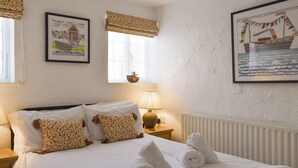 A neatly made bed with white linens, a bedside lamp, and two framed pictures on the wall.