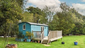 A small blue house with a wooden deck, surrounded by a grassy yard and trees. - 1 bedroom accommodation in Herstmonceux, near Hailsham (Herstmonceux, near Hailsham)