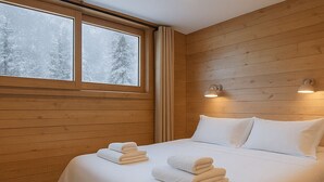 A hotel room with a wooden paneled wall, a large bed with white linens, and two bedside lamps. - Cosy chalet with views of Mont Blanc (Chamonix-Mont-Blanc)