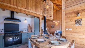 A wooden interior with a round dining table set for four, a built-in stove, and a hanging light fixture. - Cosy chalet with views of Mont Blanc (Chamonix-Mont-Blanc)