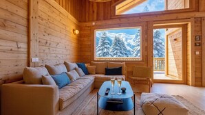 A cozy cabin interior with a wooden interior, a sofa, a coffee table with glasses, and a view of snow-covered mountains through a large window. - Cosy chalet with views of Mont Blanc (Chamonix-Mont-Blanc)