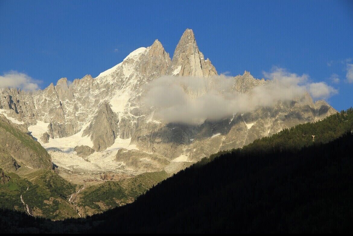 Un paisaje montañoso con un pico destacado, un valle y una zona boscosa.