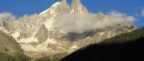 Un paisaje montañoso con un pico destacado, un valle y una zona boscosa.