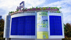 Un hotel con un letrero llamativo, amplias ventanas azules y un banderín vertical con texto.