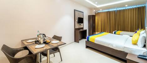 A hotel room with a bed, a desk with a chair, a table with a chair, a television, and a window with curtains.