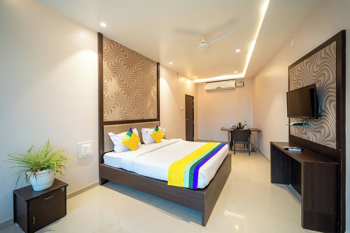 A modern hotel room with a large bed, a desk, a TV, and a ceiling fan.