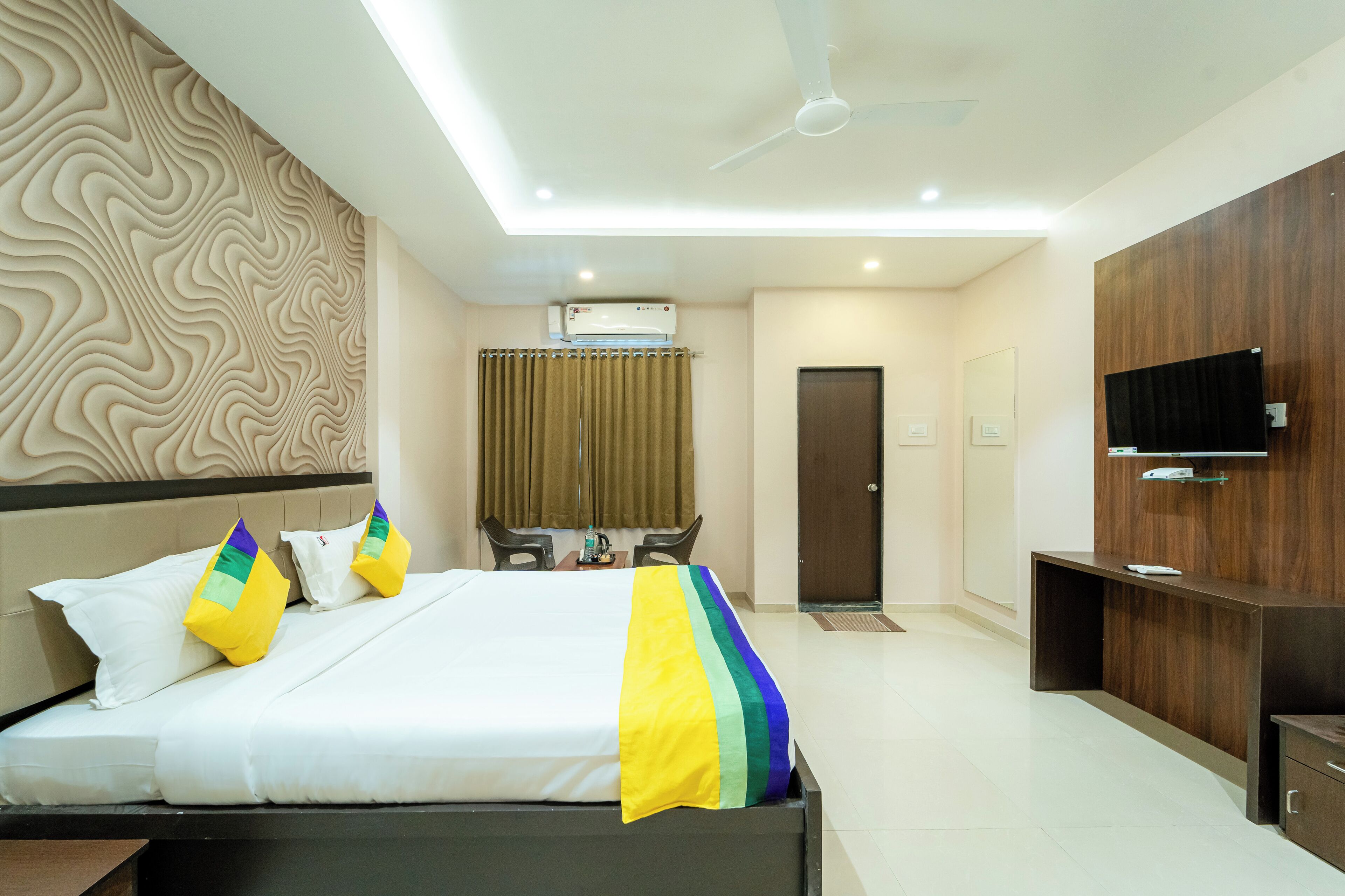 A modern hotel room with a bed, a desk, a chair, a TV, and an air conditioning unit.