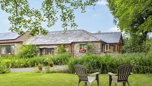 A stone house with a sloped roof, surrounded by lush greenery and a well-maintained lawn.
