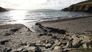A beach with rocky foreground and calm sea under a partly cloudy sky.