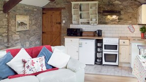 A cozy kitchen with stone walls, wooden beams, and a white refrigerator.